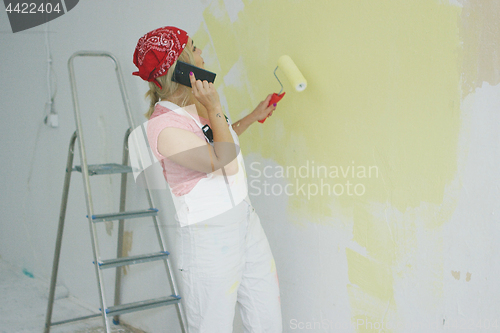 Image of Painting wall woman talking on smartphone 