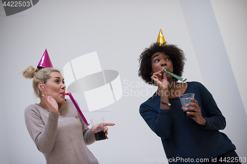 Image of smiling women in party caps blowing to whistles