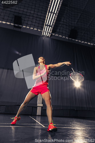 Image of Young woman playing badminton at gym