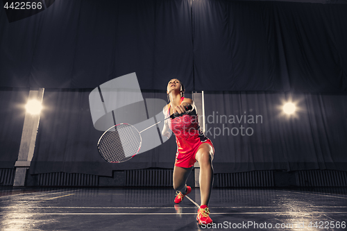 Image of Young woman playing badminton at gym