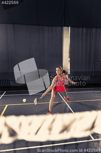 Image of Young woman playing badminton at gym