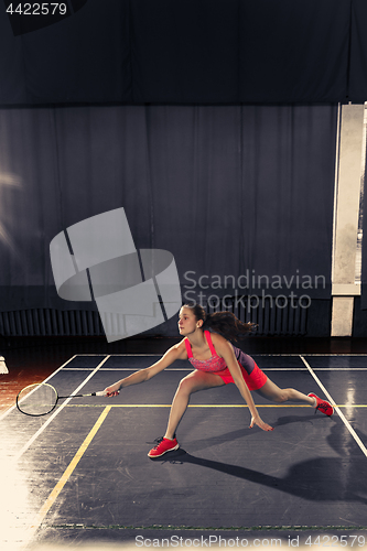 Image of Young woman playing badminton at gym