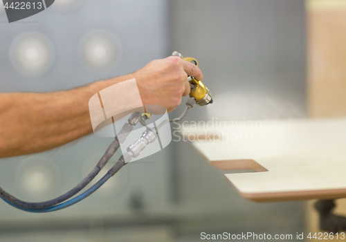 Image of worker hand sprays urethane finish to board