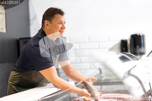 Image of male seller showing seafood at fish shop fridge