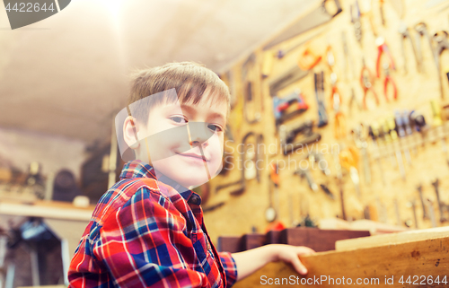 Image of happy little boy with wood plank at workshop
