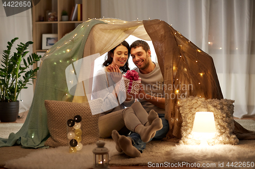 Image of happy couple with gift box in kids tent at home