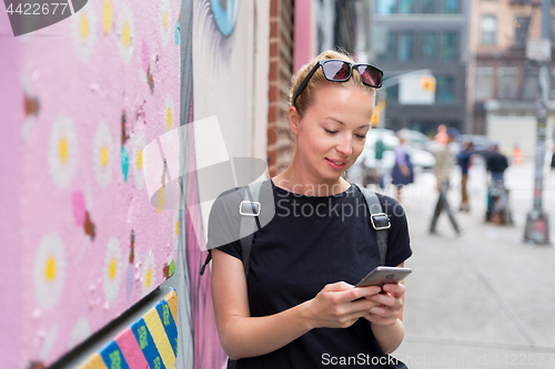 Image of Woman using smartphone against colorful graffiti wall in New York city, USA.