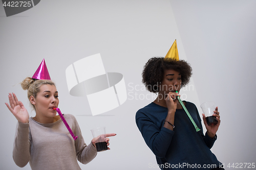 Image of smiling women in party caps blowing to whistles