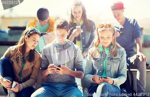 Image of happy teenage friends with smartphones outdoors
