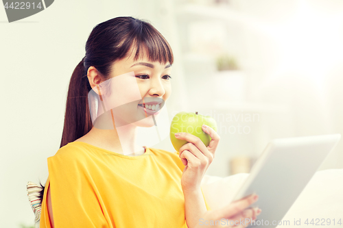 Image of happy asian woman with tablet pc and apple at home