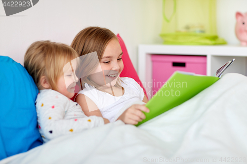 Image of little girls or sisters reading book in bed