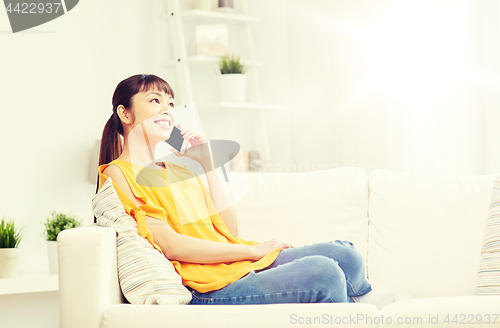 Image of happy asian woman calling on smartphone at home