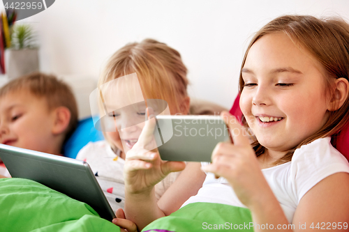 Image of happy kids with tablet pc and and smartphone in bed 