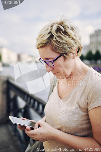 Image of Aged woman browsing smartphone on embankment