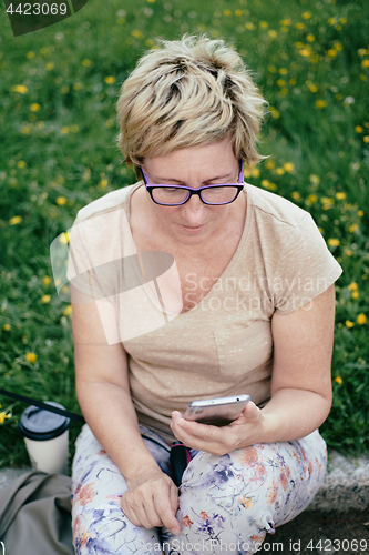 Image of Elderly woman in casual outfit, sitting on the grass in the park