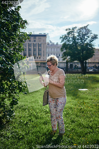 Image of Senior woman using smartphone near bush