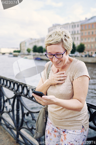 Image of Aged woman browsing smartphone on embankment