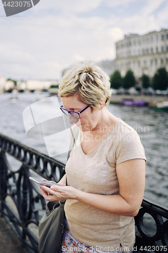 Image of Aged woman browsing smartphone on embankment