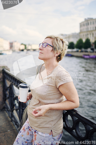 Image of Aged lady with drink on embankment