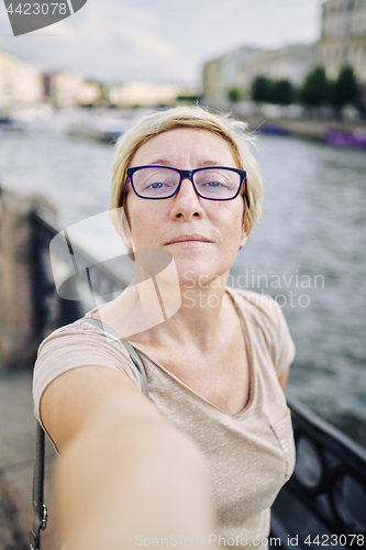 Image of Aged woman taking selfie near river