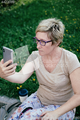 Image of Elderly woman in casual outfit, sitting on the grass in the park