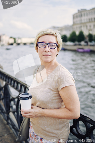 Image of Aged lady with drink on embankment