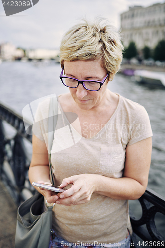 Image of Aged woman browsing smartphone on embankment