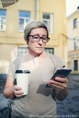 Image of Senior woman with drink using smartphone