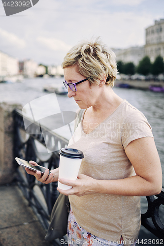 Image of Aged woman browsing smartphone on embankment