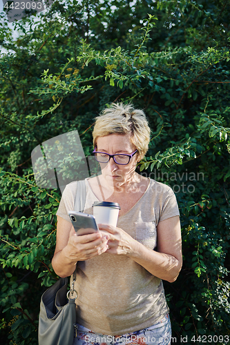 Image of Senior woman using smartphone near bush