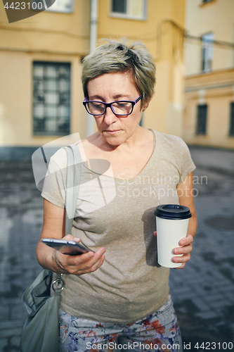 Image of Senior woman with drink using smartphone