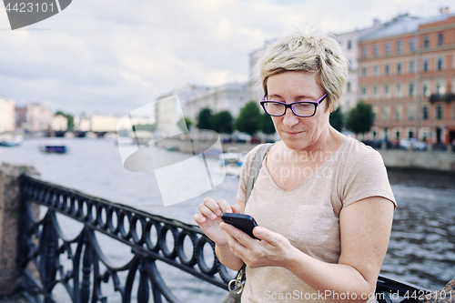 Image of Aged woman browsing smartphone on embankment