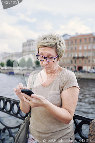 Image of Aged woman browsing smartphone on embankment