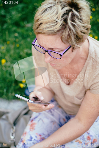 Image of Elderly woman in casual outfit, sitting on the grass in the park