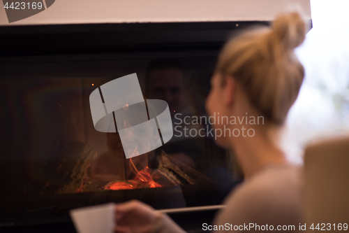 Image of young woman drinking coffee in front of fireplace