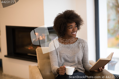 Image of black woman reading book  in front of fireplace