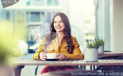 Image of happy woman drinking cocoa at city street cafe