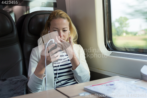 Image of Businesswoman communicating on mobile phone while traveling by train.