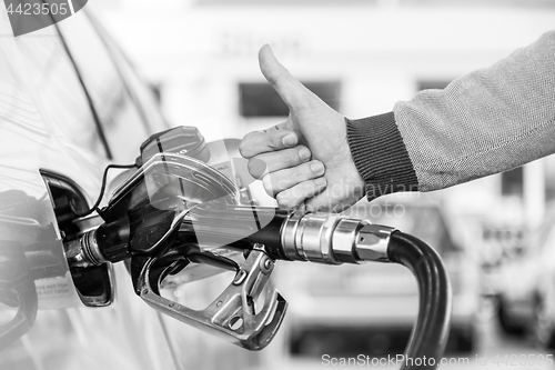 Image of Petrol or gasoline being pumped into a motor vehicle car. Closeup of man, showing thumb up gesture, pumping gasoline fuel in car at gas station.