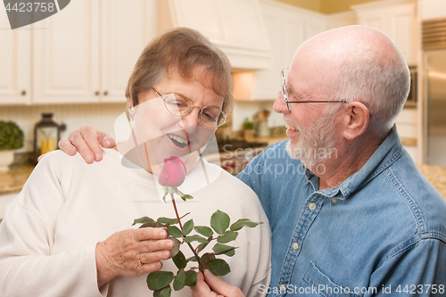 Image of Happy Senior Adult Man Giving Red Rose to His Wife Inside Kitche