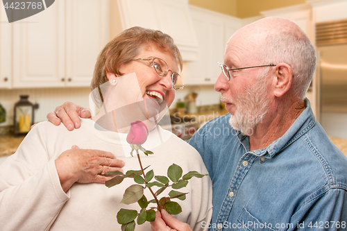 Image of Happy Senior Adult Man Giving Red Rose to His Wife Inside Kitche