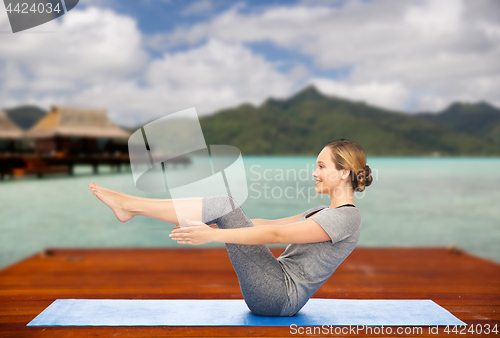 Image of woman making yoga half-boat pose on mat outdoors