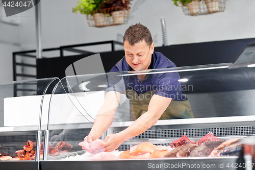 Image of male seller with seafood at fish shop fridge