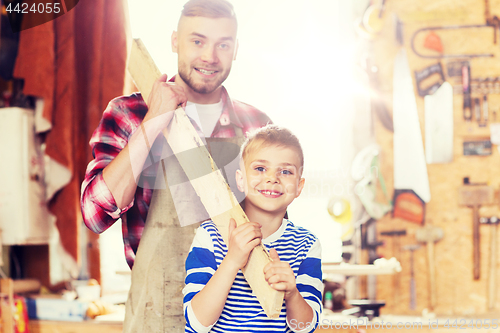 Image of happy father and son with wood plank at workshop