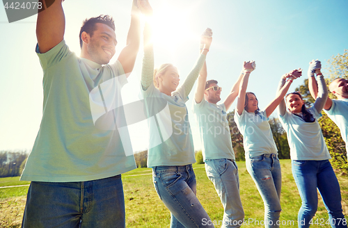 Image of group of happy volunteers holding hands outdoors