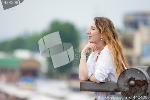 Image of A young girl looks into the distance leaning on the old fence