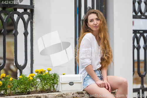 Image of A young girl with a lady\'s white handbag crouched in the alley on the street