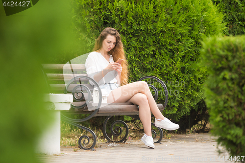 Image of Young girl communicates in social networks sitting on a park bench