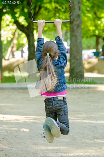 Image of A girl is riding a metal ladder on chains in a playground