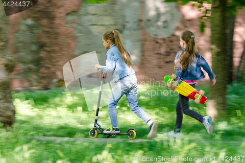 Image of The girl is riding happily on the scooter, behind her runs another girl with a skate in her hands